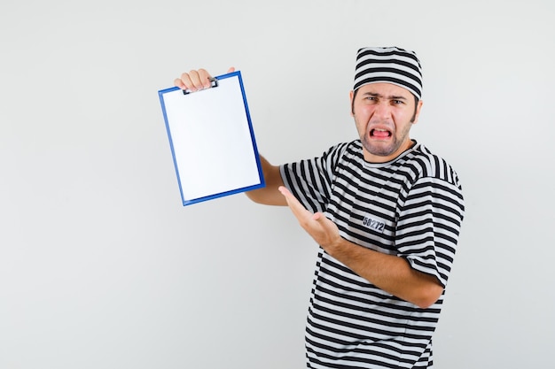 Photo gratuite jeune homme montrant le presse-papiers en t-shirt, chapeau et à la dégoûté, vue de face.