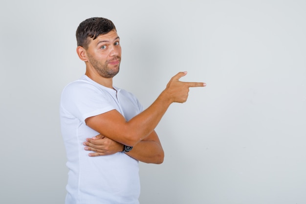 Jeune homme montrant quelque chose avec le doigt en t-shirt blanc et à la recherche de positif. .