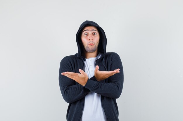 Jeune homme montrant quelque chose en t-shirt, veste et à la confusion, vue de face.