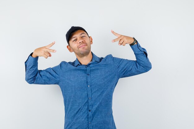 Jeune homme montrant le signe de la victoire en chemise bleue, casquette et l'air heureux, vue de face.