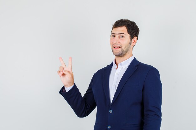 Jeune homme montrant le signe de la victoire en costume et à la joyeuse. vue de face.