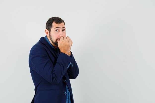 Jeune homme mordant les poings émotionnellement en chemise, veste et à la peur. vue de face.