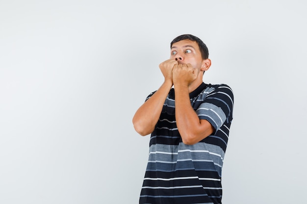 Jeune homme mordre les poings en t-shirt et à la peur, vue de face.