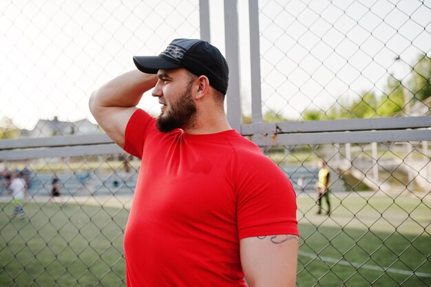 Jeune homme musclé barbu brutal portant un short et une casquette de chemise rouge au stade