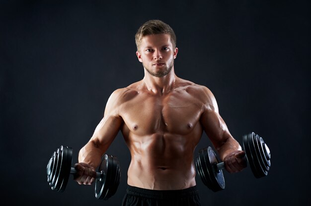 Jeune homme musclé, soulever des poids sur fond noir