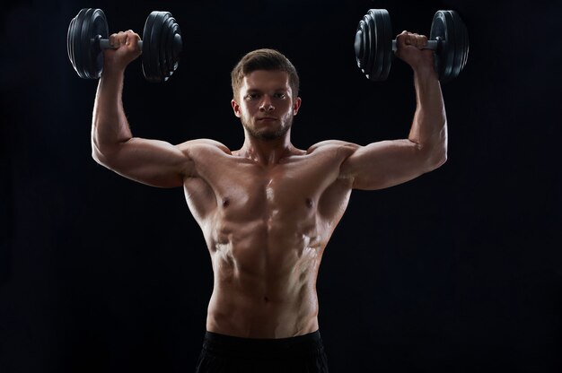 Jeune homme musclé, soulever des poids sur fond noir