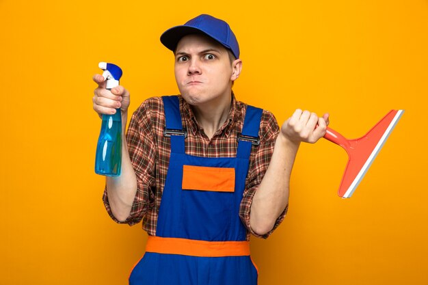 Jeune homme de nettoyage concerné portant un uniforme et une casquette tenant un agent de nettoyage avec une tête de vadrouille