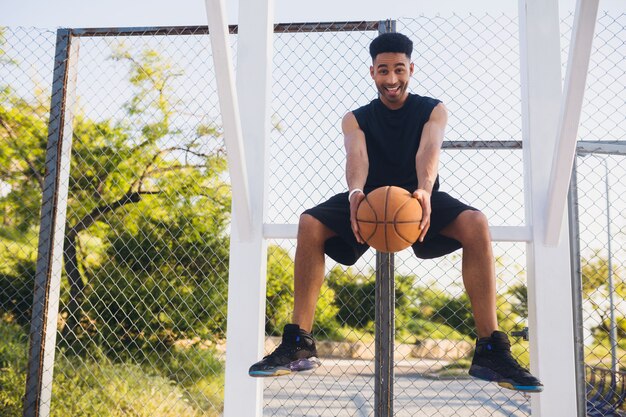 Jeune homme noir, faire du sport, jouer au basket-ball, mode de vie actif, matin d'été, souriant heureux de s'amuser