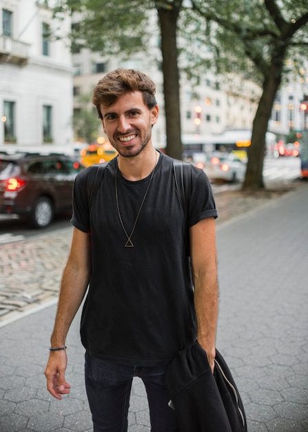 Jeune homme en noir souriant sur le trottoir