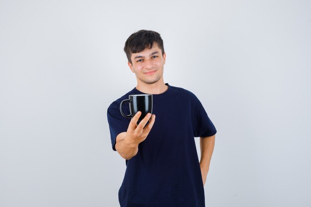 Jeune homme offrant une tasse de café en t-shirt noir et à la douce. vue de face.