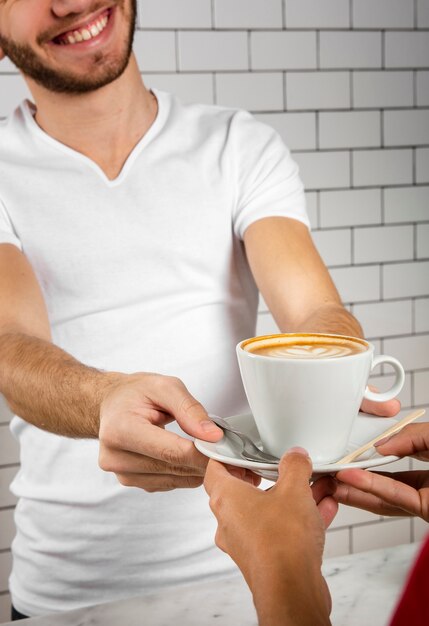 Jeune homme offrant une tasse de cappuccino