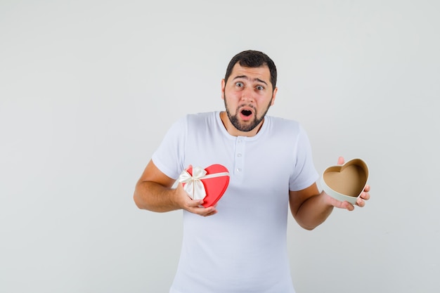 Jeune homme ouvrant la boîte présente en t-shirt blanc et regardant anxieux, vue de face.