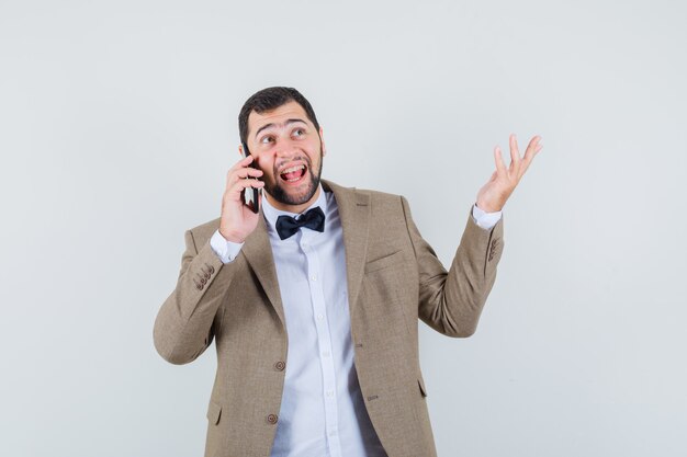 Jeune homme parlant au téléphone mobile en costume et à la vue de face, heureux.