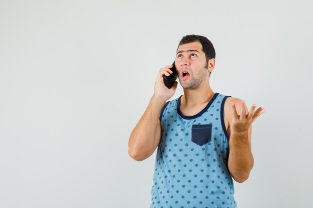 Jeune homme parlant au téléphone mobile en maillot bleu et à la confusion. vue de face.