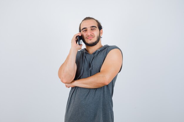 Jeune homme parlant au téléphone mobile en sweat à capuche sans manches et à la recherche de beau. vue de face.