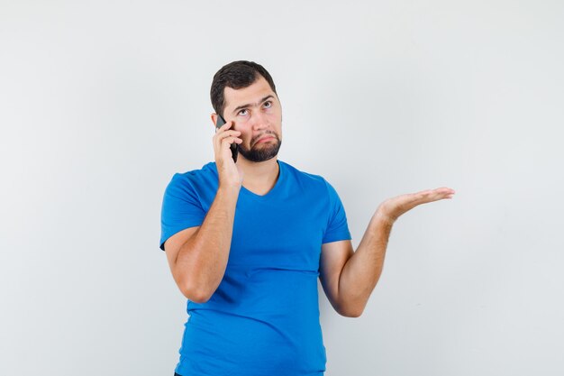 Jeune homme parlant au téléphone mobile en t-shirt bleu et à la confusion