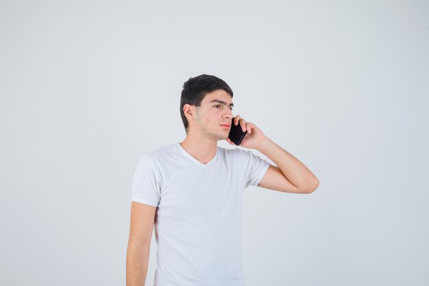 Jeune homme parlant au téléphone mobile en t-shirt et à la confiance. vue de face.