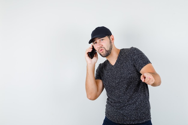 Jeune homme parlant au téléphone mobile tout en pointant vers l'extérieur en t-shirt et casquette