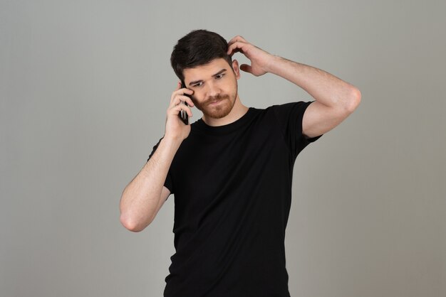 Jeune homme parlant avec téléphone sur un gris.