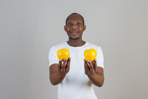 Jeune homme à la peau foncée tenant des fruits de coing mûrs sur un mur gris