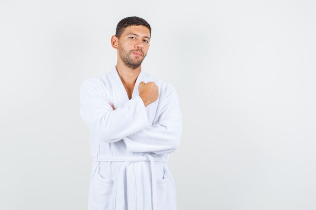 Jeune homme en peignoir blanc gardant le poing serré et à la vue de face, confiant.