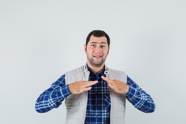 Jeune homme pinçant son col en chemise, veste sans manches et à l'ennui. vue de face.