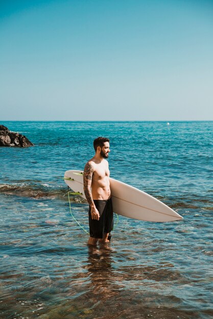 Jeune homme avec planche de surf dans l&#39;eau