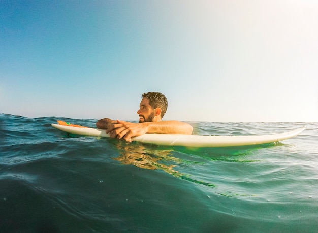 Jeune homme avec planche de surf en mer bleue
