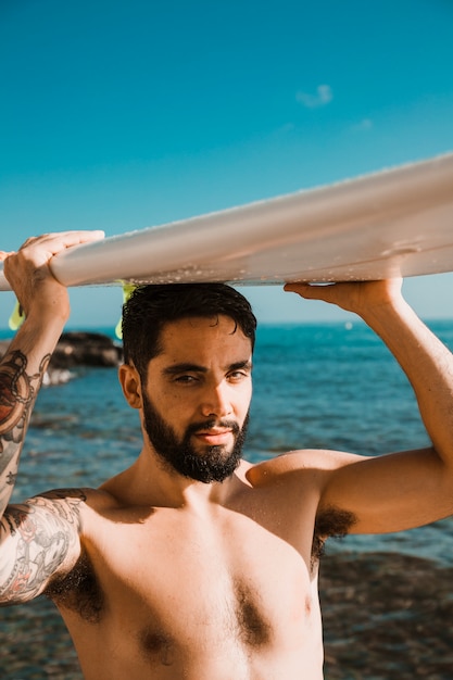 Photo gratuite jeune homme, à, planche surf, sur, tête, sur, plage, mer, et, ciel bleu