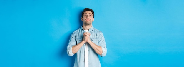 Jeune homme plein d'espoir levant les yeux et priant Dieu implorant de l'aide debout sur fond bleu