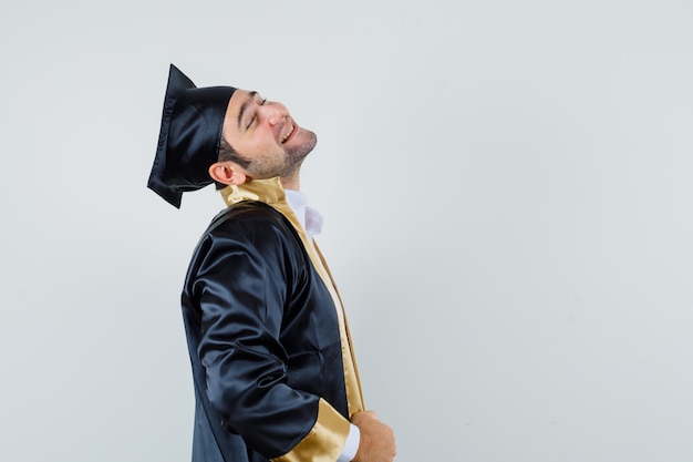 Photo gratuite jeune homme pliant la tête en arrière en uniforme d'études supérieures et à la recherche de calme.