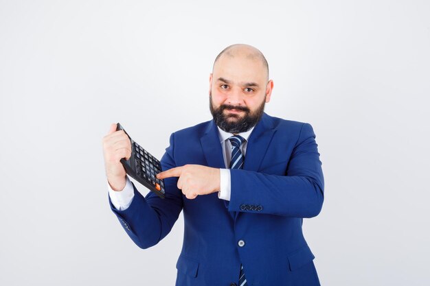 Jeune homme pointant sur la calculatrice en chemise blanche, veste et à l'air confiant. vue de face.