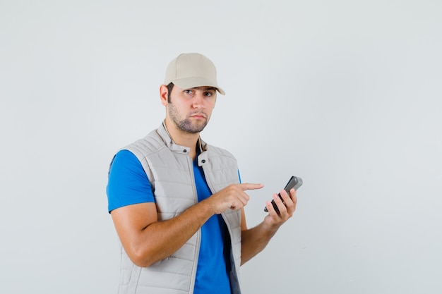 Jeune homme pointant sur la calculatrice en t-shirt, veste et regardant pensif, vue de face.
