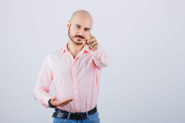 Jeune homme pointant sur la caméra en chemise rose, vue de face de jeans.