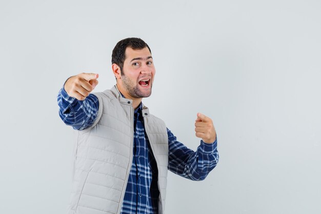 Jeune homme pointant la caméra en chemise, veste sans manches et à la jolly, vue de face.