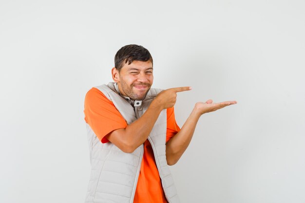 Jeune homme pointant de côté, faisant semblant de tenir quelque chose d'autre part en t-shirt, veste et à la joyeuse