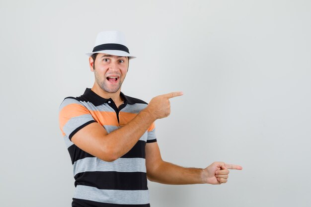 Jeune homme pointant de côté en t-shirt, chapeau et à l'espace heureux pour le texte