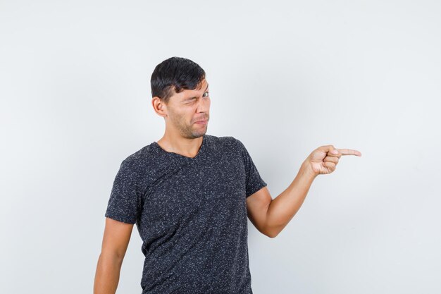 Jeune homme pointant de côté en t-shirt noir et l'air perplexe. vue de face.