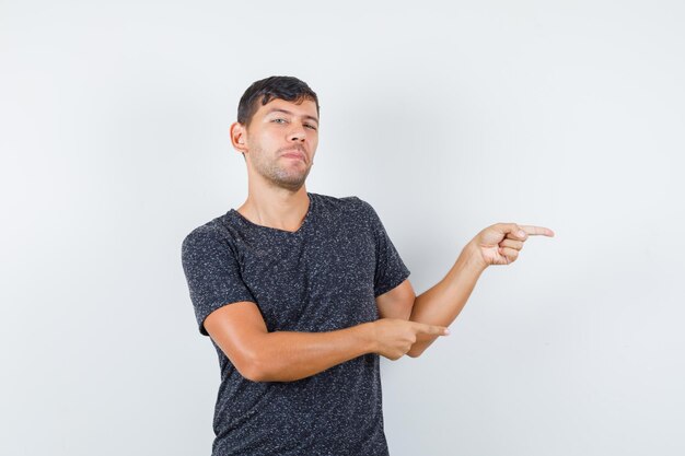 Jeune homme pointant de côté en t-shirt noir et ayant l'air assuré, vue de face.