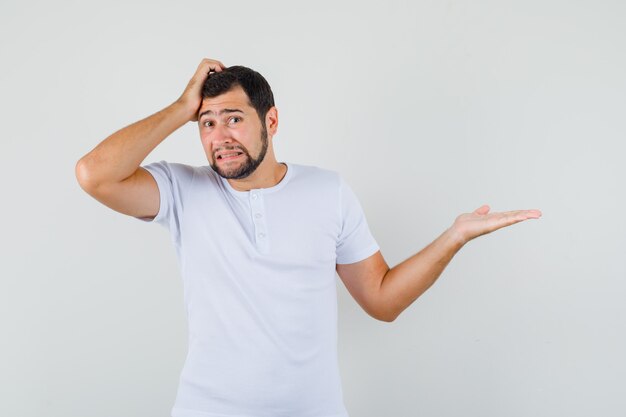 Jeune homme pointant de côté en t-shirt et à la troublé. vue de face.