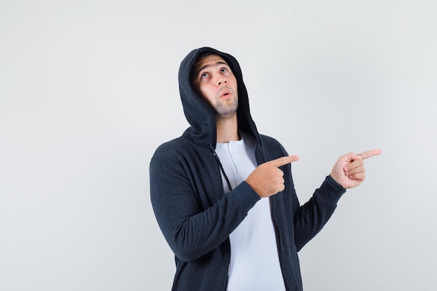 Jeune homme pointant de côté en t-shirt, veste et regardant pensif, vue de face.