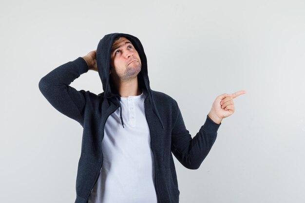 Jeune homme pointant de côté en t-shirt, veste et à la vue de face, hésitante.