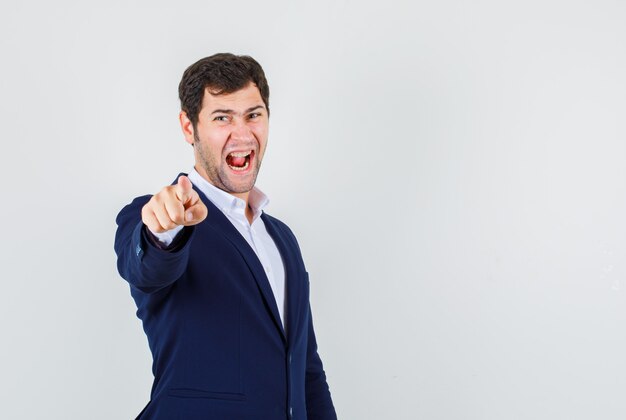 Jeune homme pointant le doigt en criant en costume et à la nervosité. vue de face.