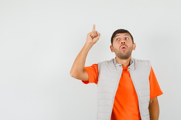 Jeune homme pointant le doigt vers le haut en t-shirt, veste et regardant concentré. vue de face.