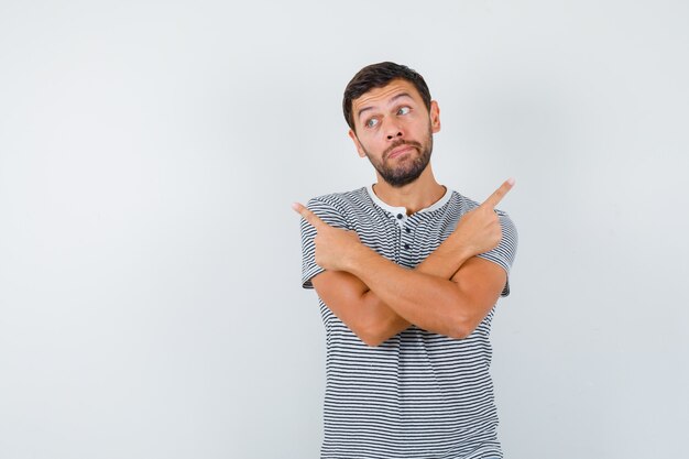 Jeune homme pointant à droite et à gauche, regardant loin en t-shirt et ayant l'air indécis, vue de face.