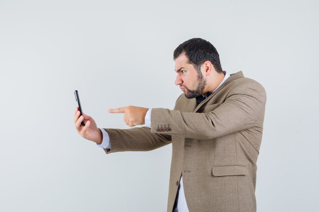 Jeune homme pointant sur l'écran sur le chat vidéo en costume et à la colère, vue de face.