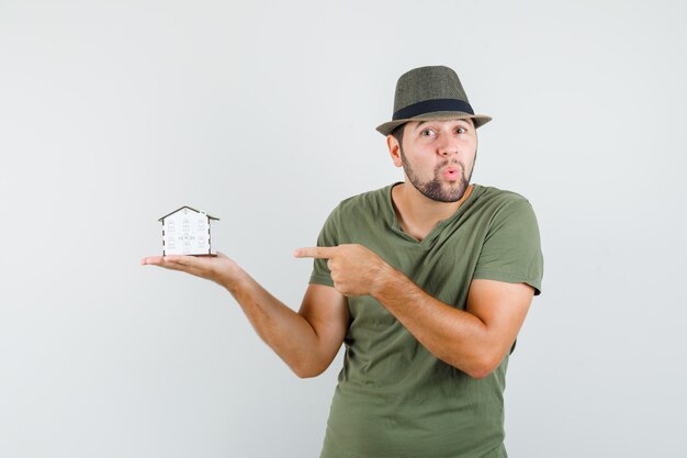 Jeune homme pointant sur le modèle de la maison en t-shirt vert et chapeau et à la surprise