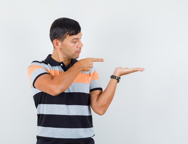 Jeune homme pointant sur la paume écartée en t-shirt et à la recherche concentrée