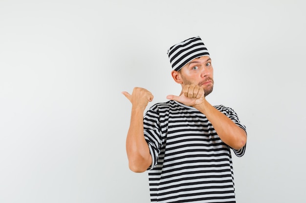 Jeune homme pointant les pouces vers l'arrière en chapeau t-shirt rayé et à la confusion