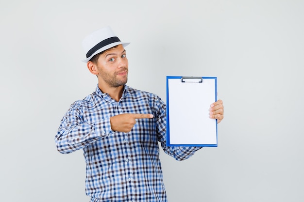 Photo gratuite jeune homme pointant sur le presse-papiers en chemise à carreaux, chapeau et à la confiance.